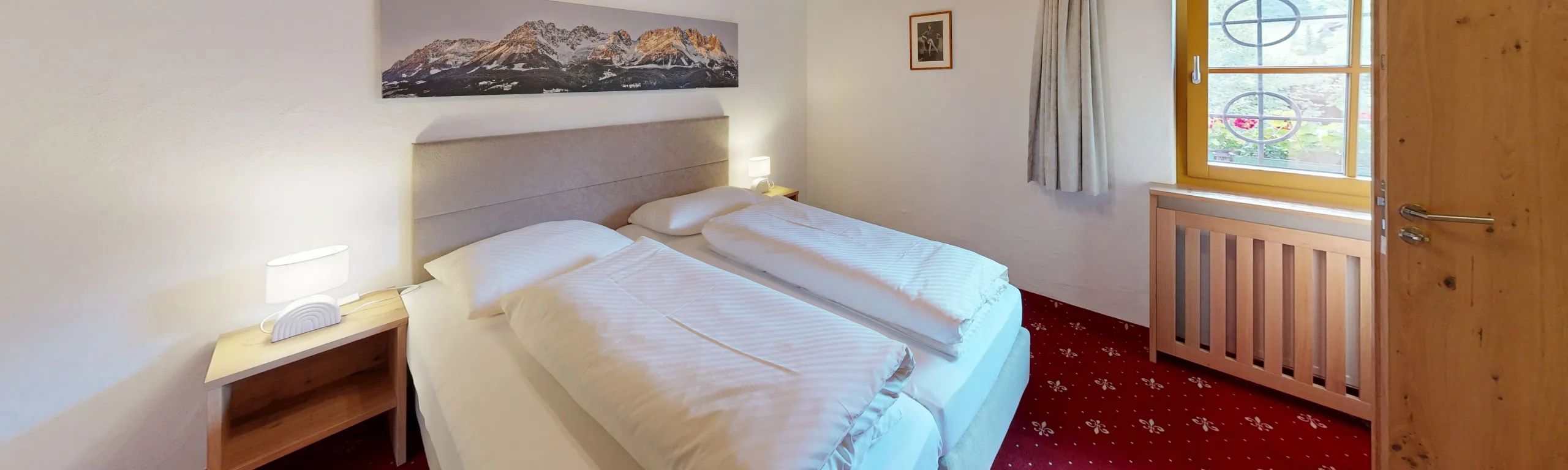 Helles Schlafzimmer mit zwei Betten, Fenster und Holzmöbeln.