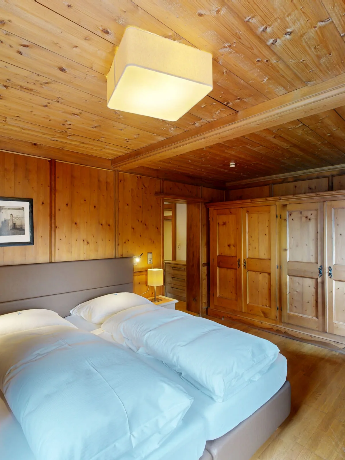 Holzvertäfeltes Schlafzimmer mit zwei Betten, Kommode und gemütlicher Ausstattung.