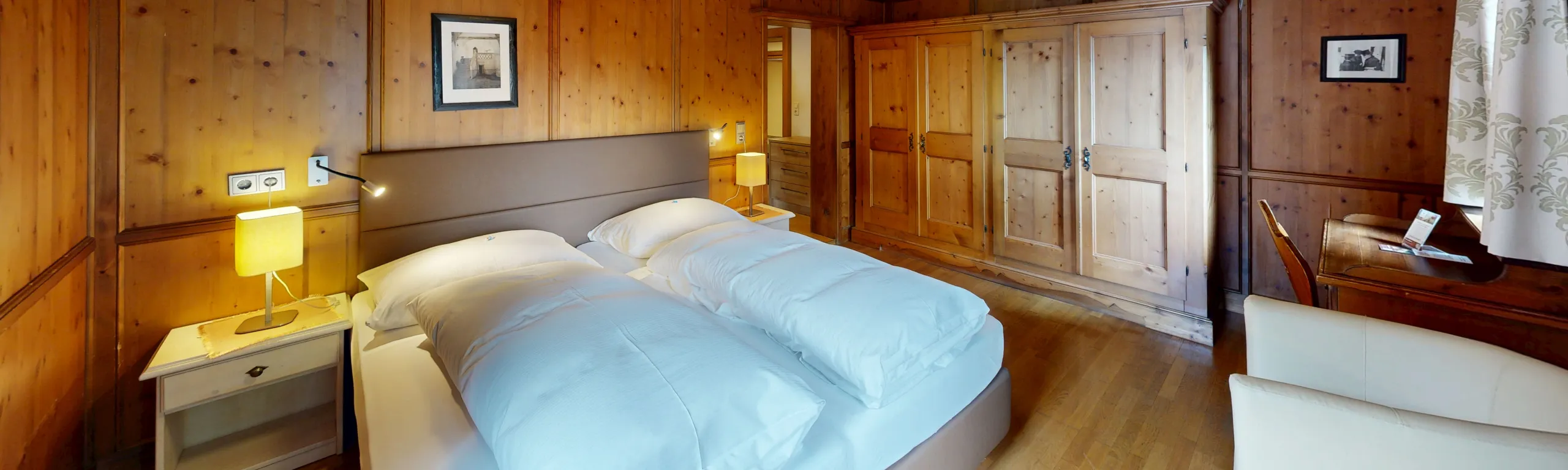 Gemütliches Zimmer mit Holzverkleidung, Bett und Licht neben Nachttisch.